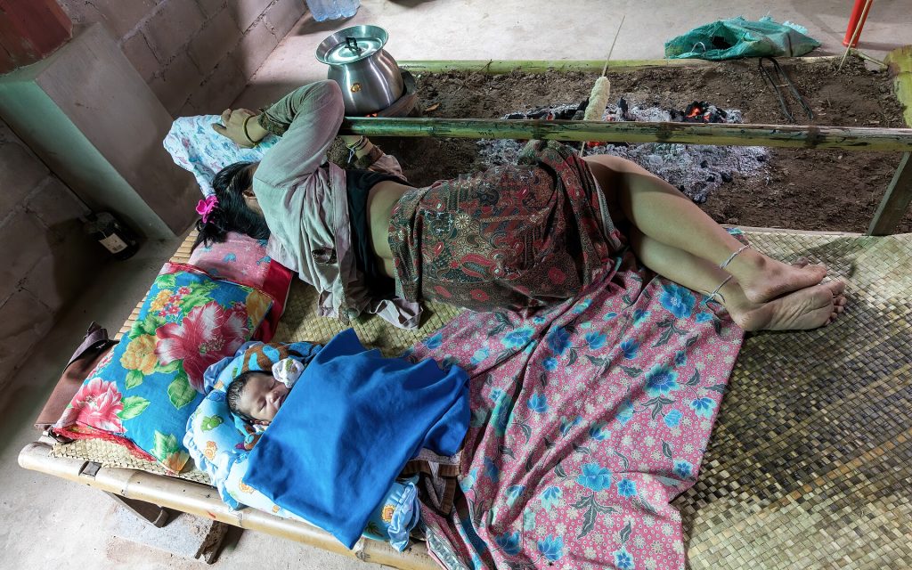 A mother and newborn baby sleeping on a bamboo bed in Laos